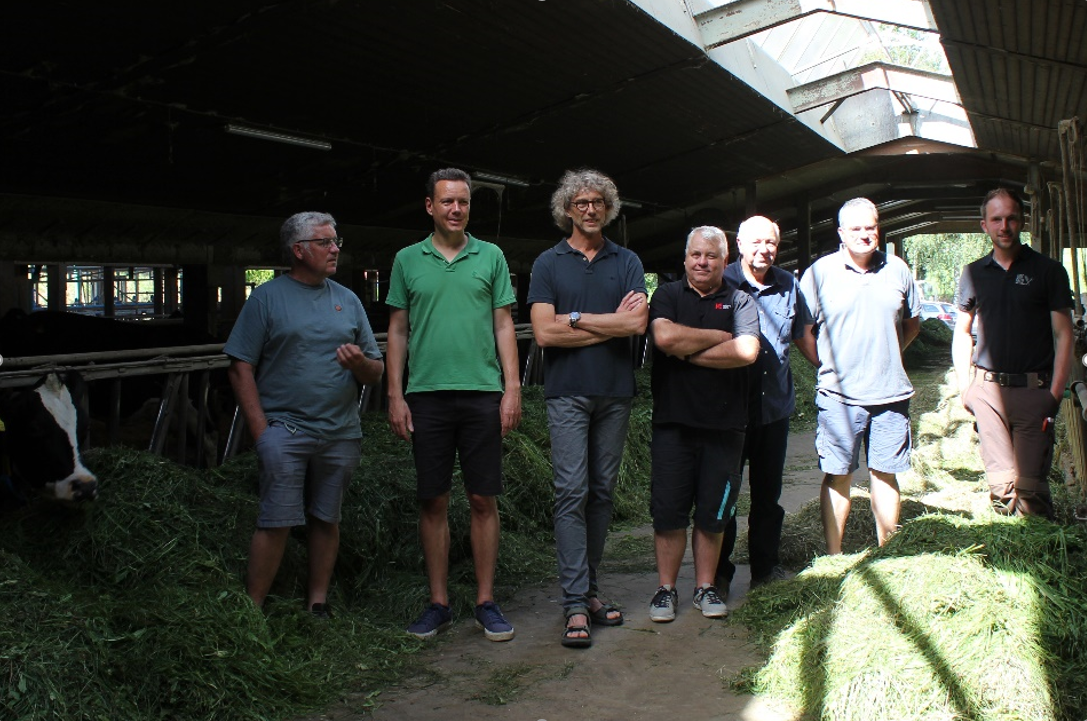 zu sehen sind die Beteiligten des Projektes mit Landrat Harald Sievers im Stall von Jakob Sigg zwischen Kühen die frisches Gras fressen. 