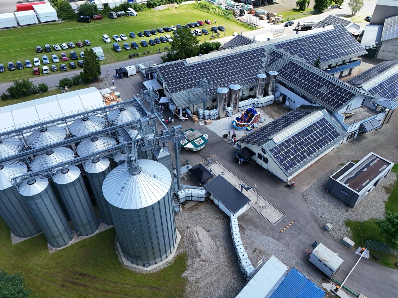 Die Firma dreher bio sieht man von oben, auf der Wiese daneben sieht man die Autos der Besucher, im Innenhof der Gebäude steht eine Hüpfburg und der Getränkewagen der Brauerei Härle